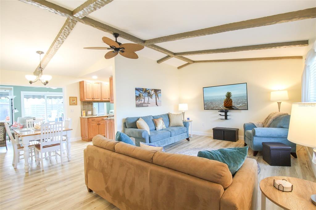 A living room and dining area feature wood-look flooring, exposed ceiling beams, and blue furniture — 3852 GATEWOOD DRIVE, SARASOTA, FL