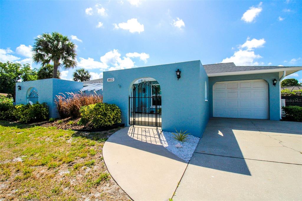A light blue house features a gated courtyard entrance, a single-car garage, and palm trees — 3852 GATEWOOD DRIVE, SARASOTA, FL