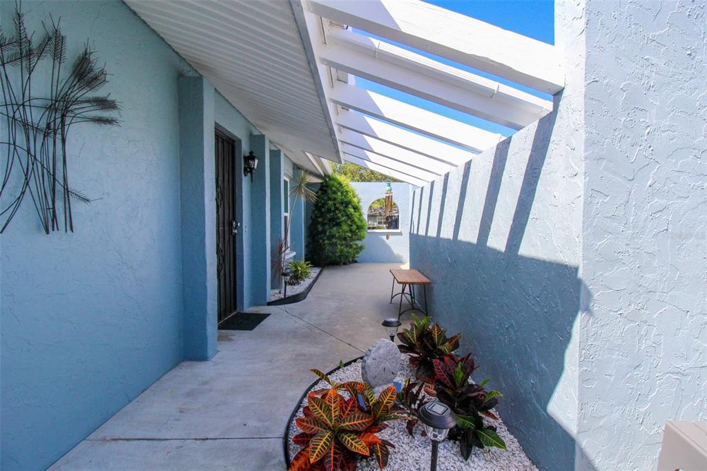 A blue-walled outdoor walkway features a white pergola roof, a small bench, and landscaping — 3852 GATEWOOD DRIVE, SARASOTA, FL