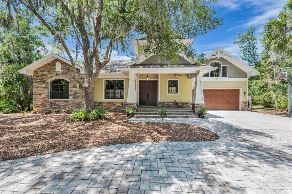 A front exterior view of a house featuring a stone facade, porch, and double doors — 5911 RIVER FOREST CIRCLE, BRADENTON, FL