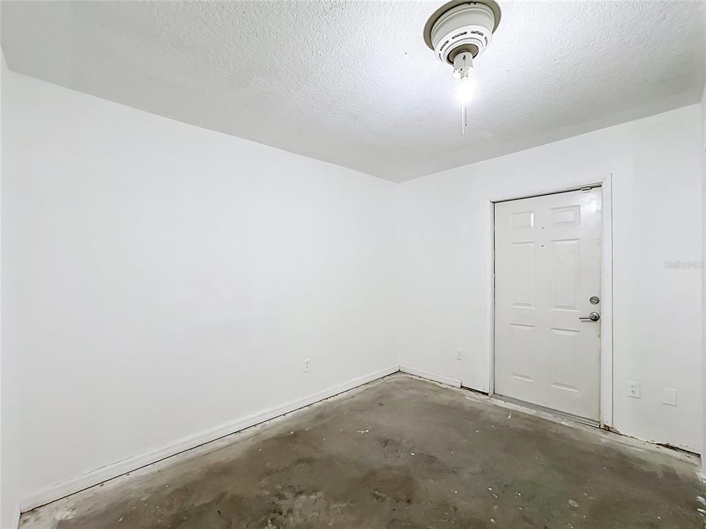 An unfinished room with white walls, a concrete floor, and a single white entry door — 1126 15TH AVENUE SW, VERO BEACH, FL