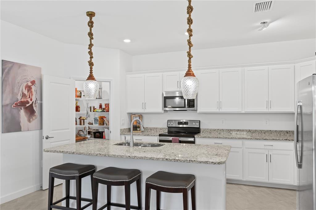 A kitchen features white cabinets, granite countertops, a center island with bar stools, and pendant lights — 3390 WESTON MANOR DRIVE, ALVA, FL