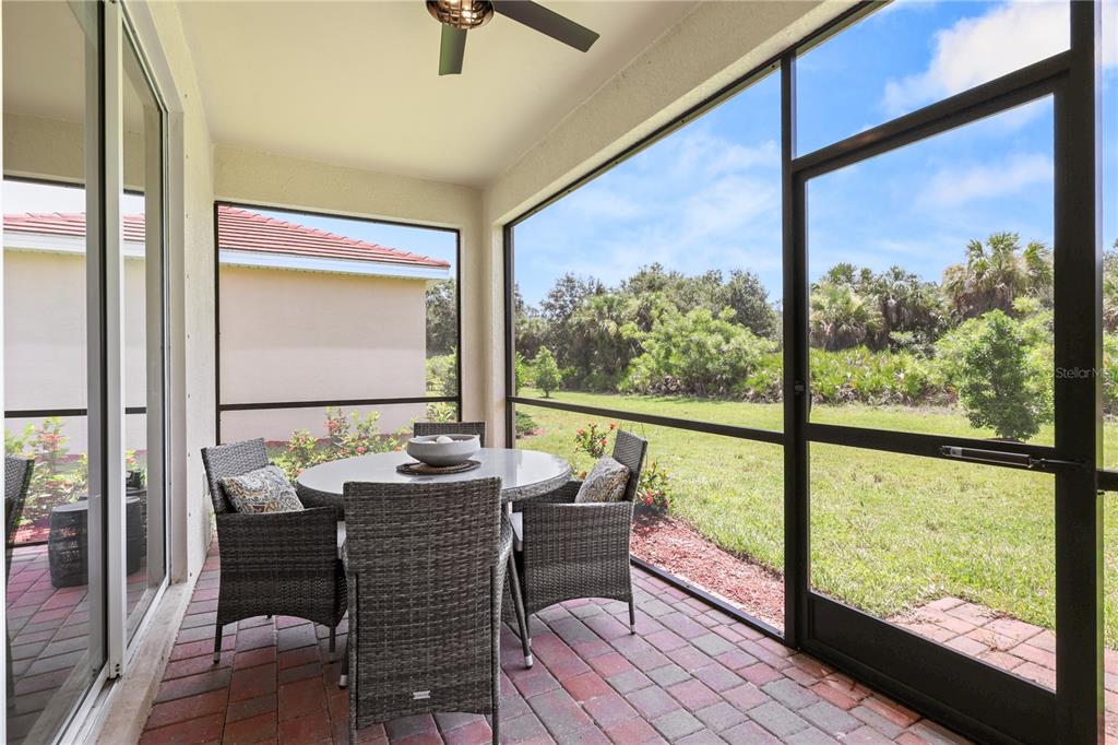 A screened-in patio with a dining set overlooks a grassy backyard and wooded area — 3390 WESTON MANOR DRIVE, ALVA, FL