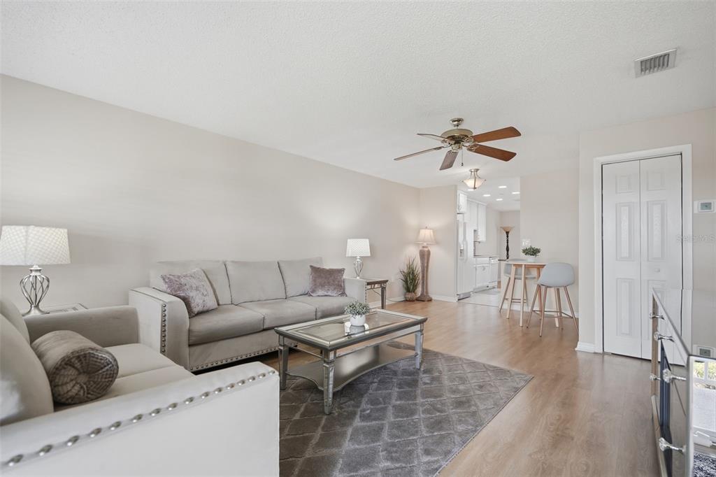 A living room features light-colored walls, wood-look flooring, a gray sofa, and a ceiling fan — 10033 64TH AVENUE N UNIT 16, ST PETERSBURG, FL