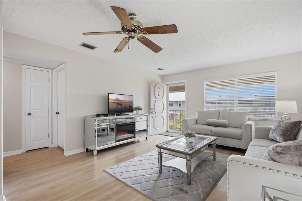 A living room with light wood floors, a mirrored media console, and a grey sofa — 10033 64TH AVENUE N UNIT 16, ST PETERSBURG, FL