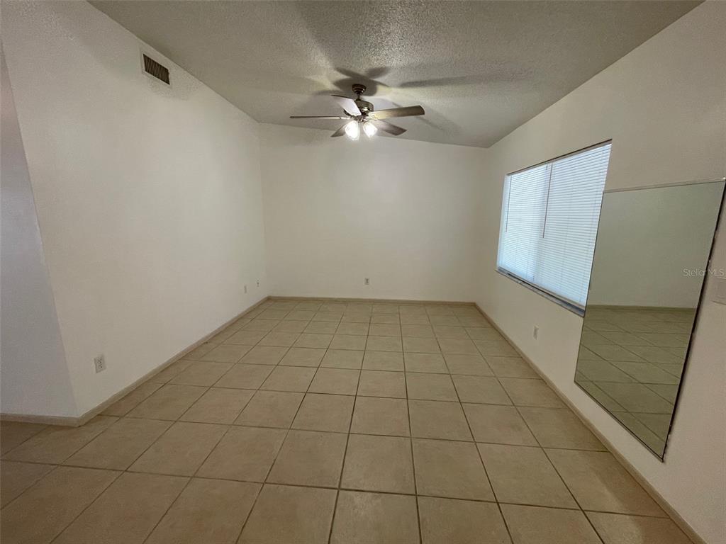 An empty room features beige tile flooring, white walls, a ceiling fan, and a wall mirror — 9000 GRIGGS ROAD UNIT C, ENGLEWOOD, FL