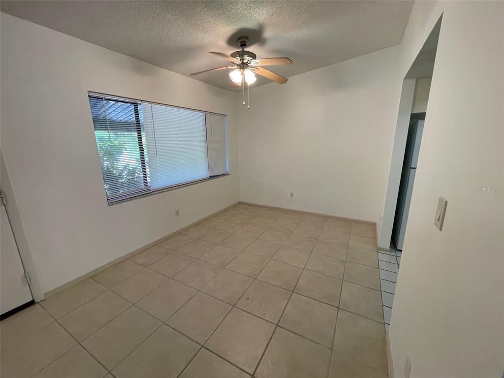 An empty room with beige tile flooring, a ceiling fan, and a large window — 9000 GRIGGS ROAD UNIT C, ENGLEWOOD, FL