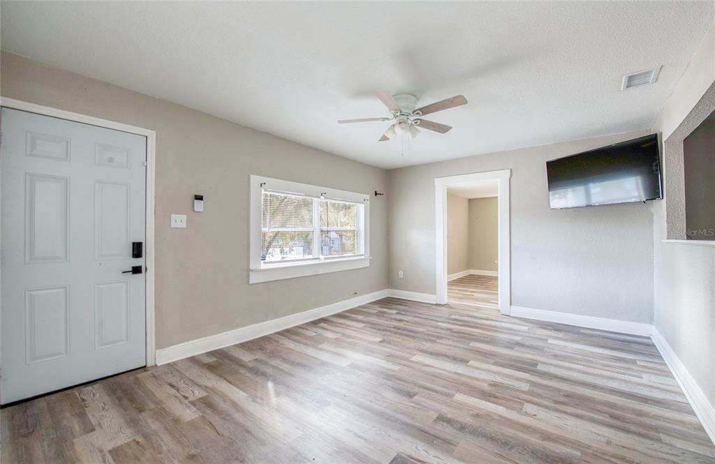A living room features light gray walls, wood-look flooring, a ceiling fan, and a wall-mounted television — 1516 E WATERS AVENUE, TAMPA, FL