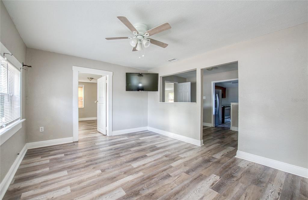 A living room features light gray walls, wood-look flooring, a ceiling fan, and a television — 1516 E WATERS AVENUE, TAMPA, FL