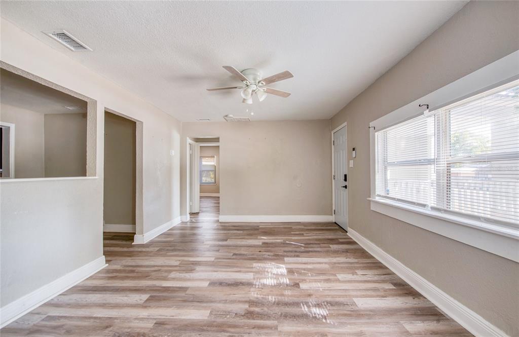 An empty living room features light-colored walls, wood-look flooring, a ceiling fan, and a window — 1516 E WATERS AVENUE, TAMPA, FL