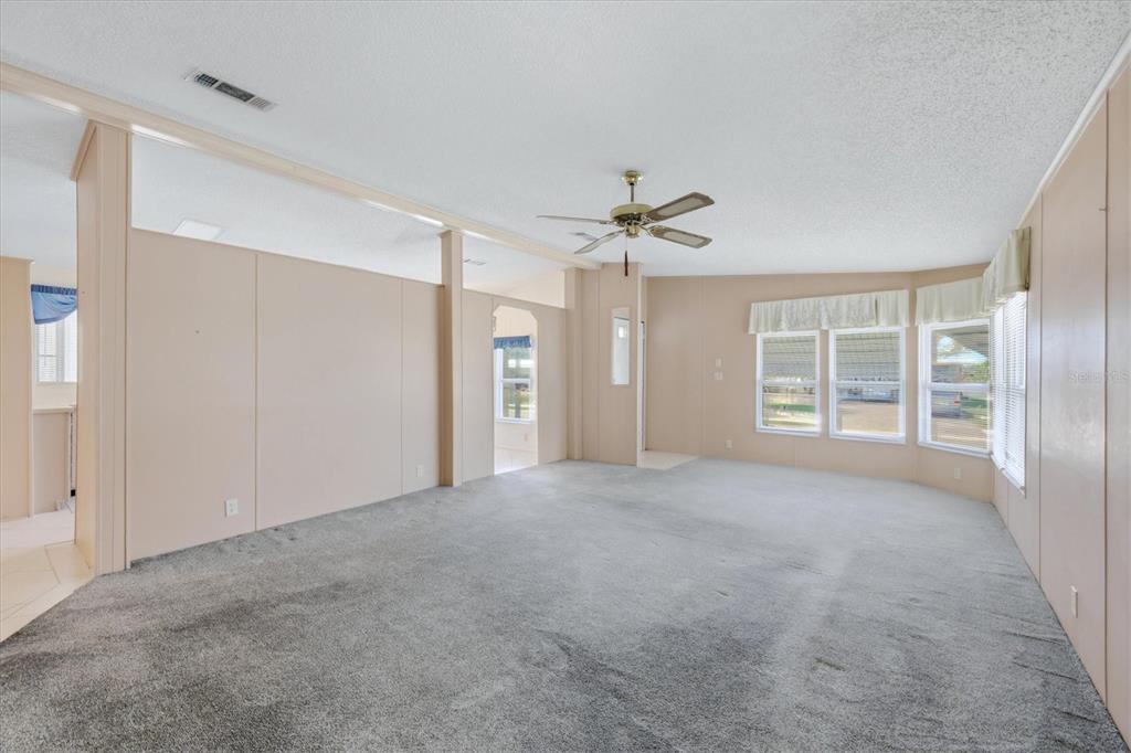 A spacious living room features beige paneled walls, gray carpeting, and a ceiling fan — 8420 IMPERIAL CIRCLE, PALMETTO, FL