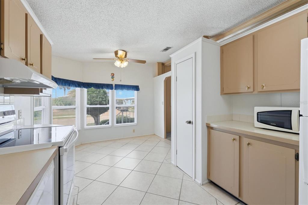 A kitchen with tan cabinets, white appliances, tile flooring, and a dining area with windows — 8420 IMPERIAL CIRCLE, PALMETTO, FL