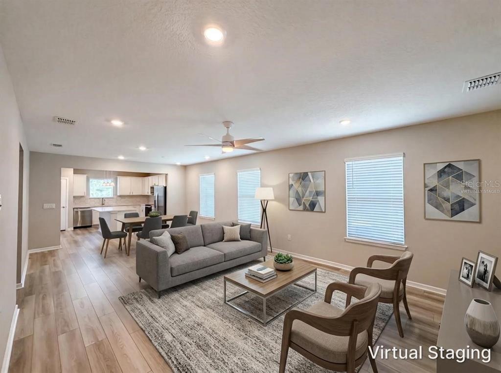 A living room with wood-look flooring, a gray sofa, and an open kitchen in the background — 8332 SW 54TH LOOP, OCALA, FL