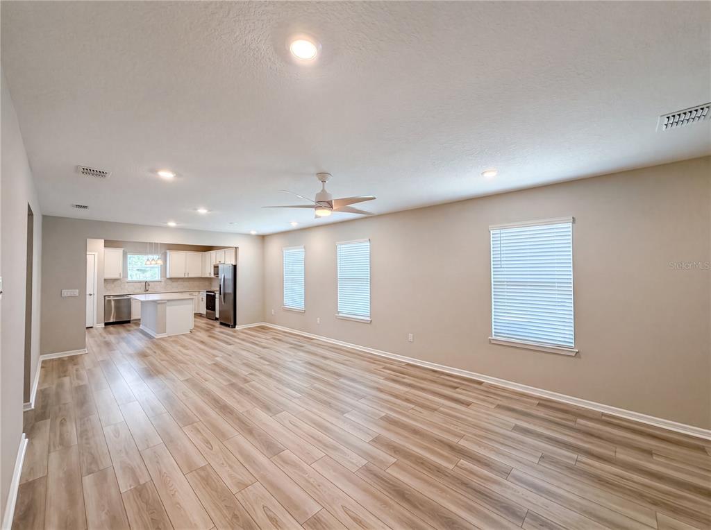An open-concept living area features light wood-look flooring, beige walls, and an adjacent kitchen — 8332 SW 54TH LOOP, OCALA, FL