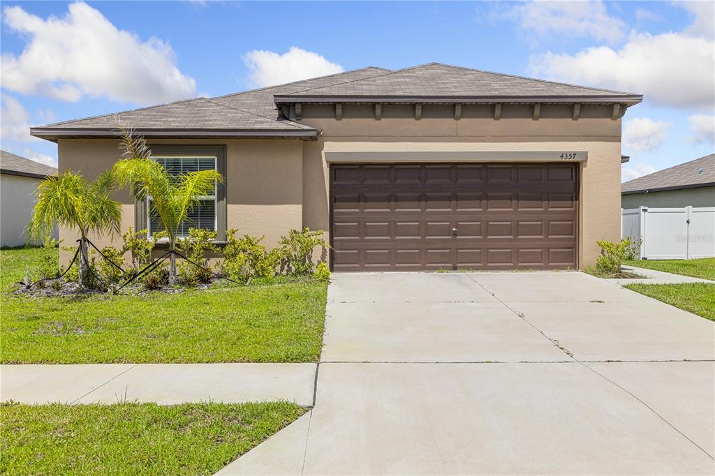 A single-story house with a tan stucco exterior, a brown garage door, and a palm tree — 4357 FABULOUS FINCH LANE, BARTOW, FL