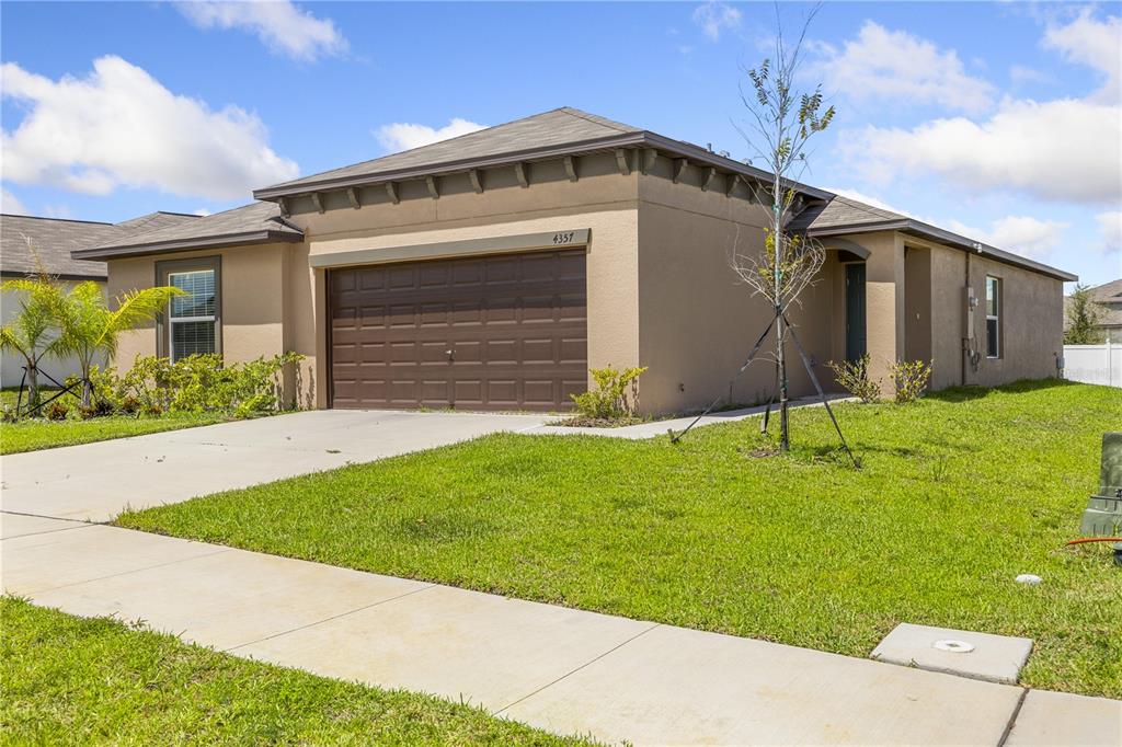 A tan single-story house with a brown garage door and a concrete driveway — 4357 FABULOUS FINCH LANE, BARTOW, FL