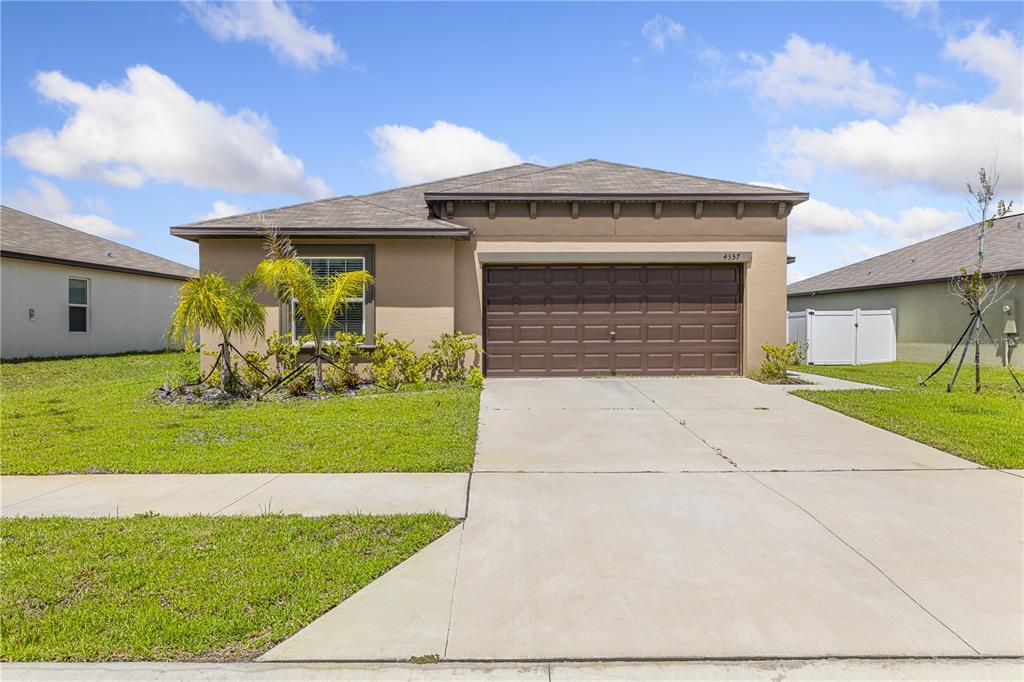 A single-story house with a tan stucco exterior, a brown garage door, and a concrete driveway — 4357 FABULOUS FINCH LANE, BARTOW, FL