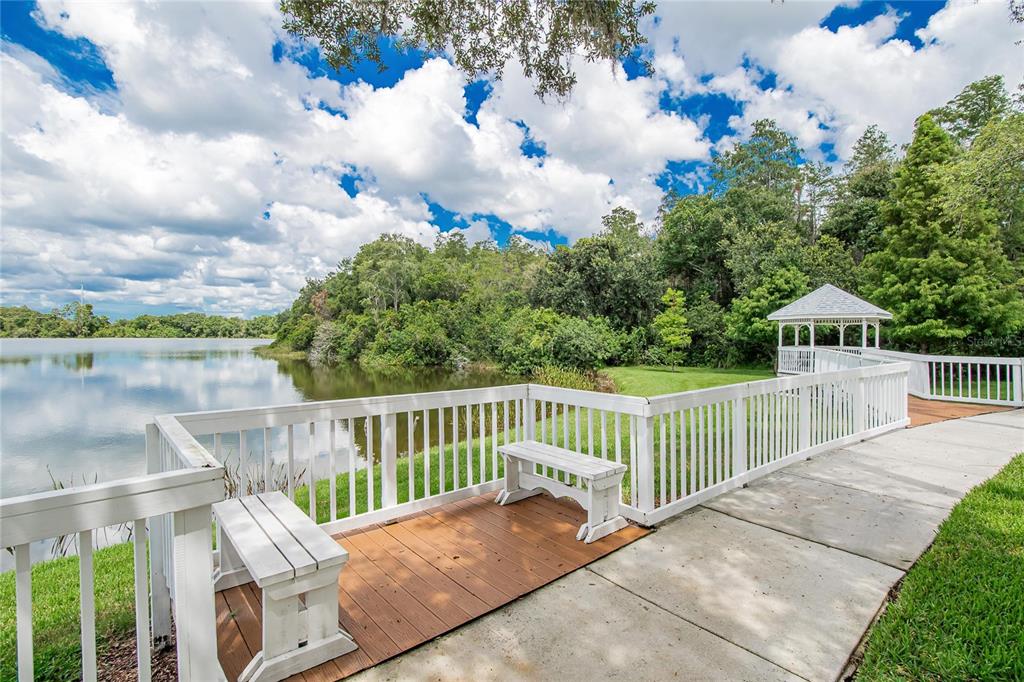 A white wooden railing surrounds a wooden deck with benches overlooking a lake and gazebo — 10807 SIERRA VISTA PLACE, TAMPA, FL