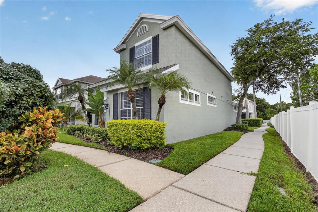 A two-story light green house with dark shutters sits beside a sidewalk and white fence — 10807 SIERRA VISTA PLACE, TAMPA, FL