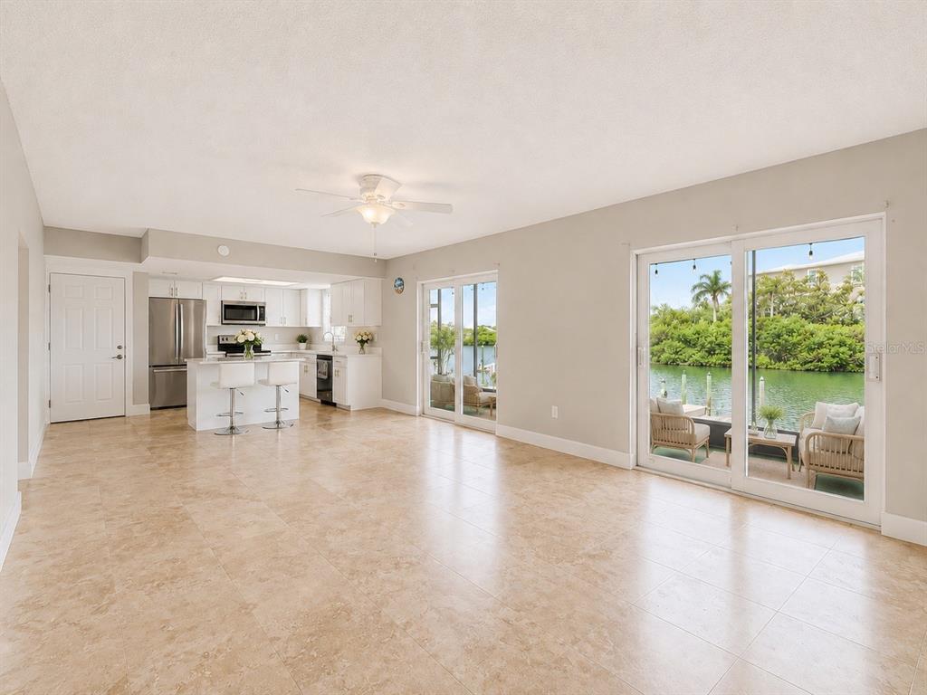 An open-concept living area features light tile flooring, a kitchen with white cabinetry, and waterfront views — 8818 BAY POINTE DRIVE UNIT 108, TAMPA, FL