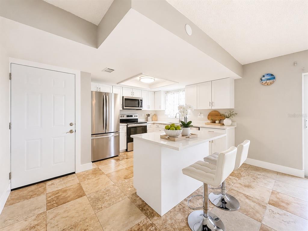 A kitchen features white cabinets, stainless steel appliances, a central island, and tiled flooring — 8818 BAY POINTE DRIVE UNIT 108, TAMPA, FL