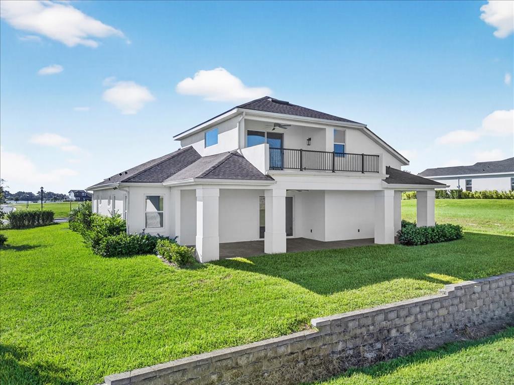 A two-story house with a covered patio, a second-floor balcony, and a stone retaining wall — 200 SNOWY ORCHID WAY, LAKE ALFRED, FL
