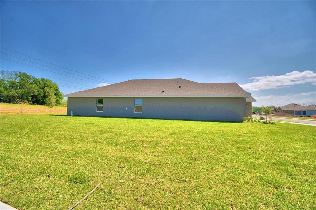 The exterior side view of a single-story house features a gray stucco wall and lawn — 3644 LINDBERGH STREET, LAKELAND, FL