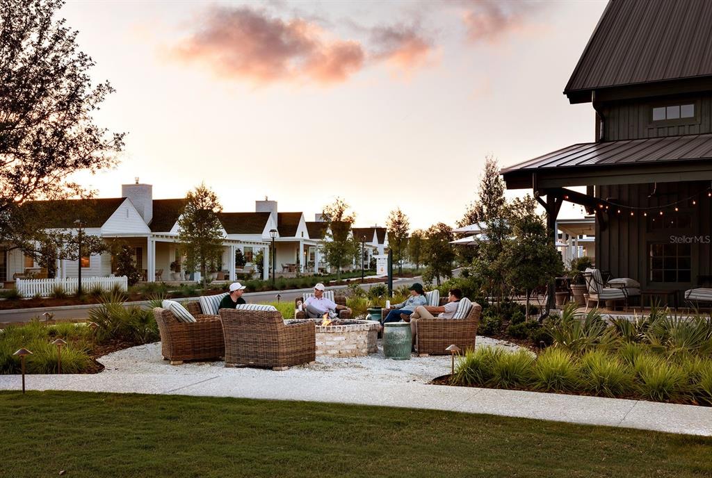 People sit around a stone fire pit on a patio outside a dark-sided building — 18381 SPLIT RAIL RD, BROOKSVILLE, FL