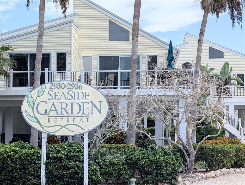 A yellow multi-story building with a balcony stands behind a Seaside Garden Retreat sign — 2934 GULF OF MEXICO DRIVE UNIT 2934, LONGBOAT KEY, FL