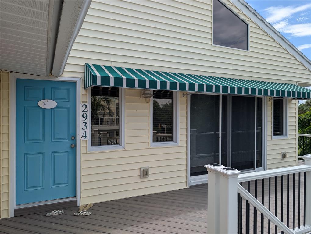 A light yellow house exterior features a blue door, green striped awning, and wooden deck — 2934 GULF OF MEXICO DRIVE UNIT 2934, LONGBOAT KEY, FL