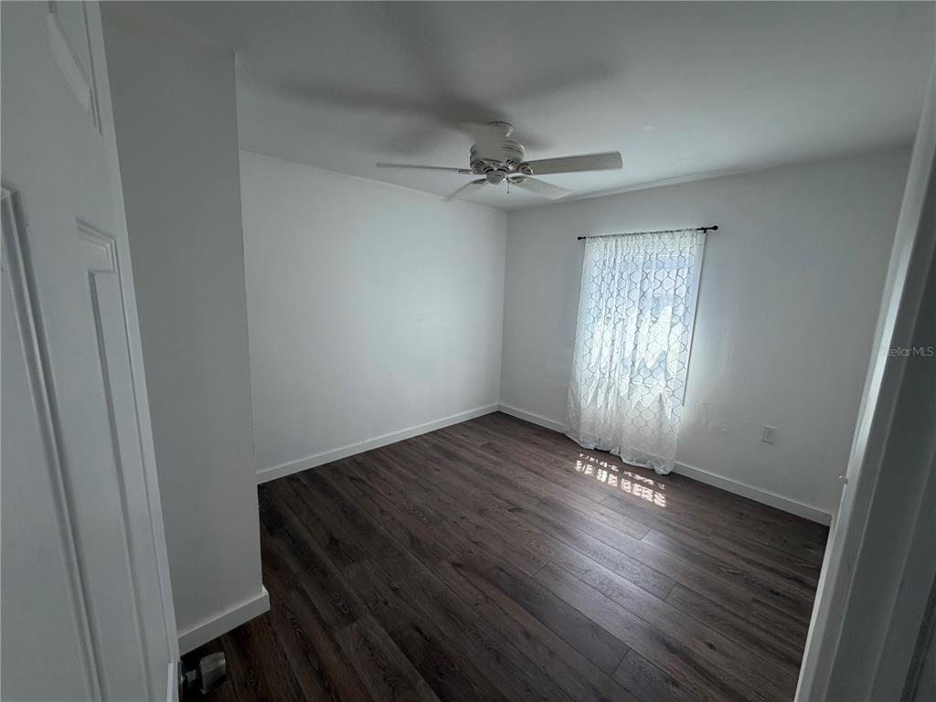 A bedroom with white walls, dark wood-look flooring, a ceiling fan, and an open closet — 911 N 21ST STREET, FORT PIERCE, FL