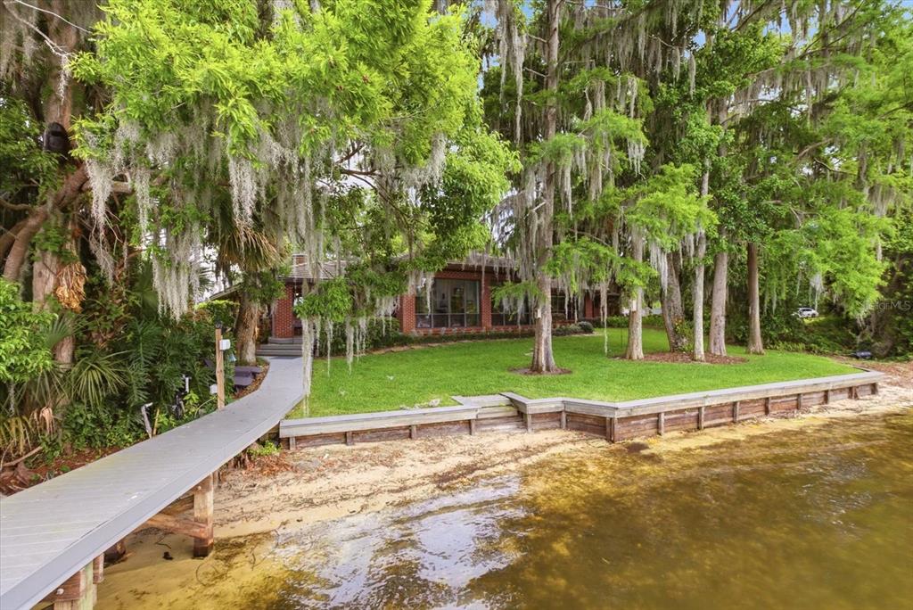 An aerial view shows a house and a large vacant lot bordering a lake — 4910 E LAKE DRIVE, WINTER SPRINGS, FL