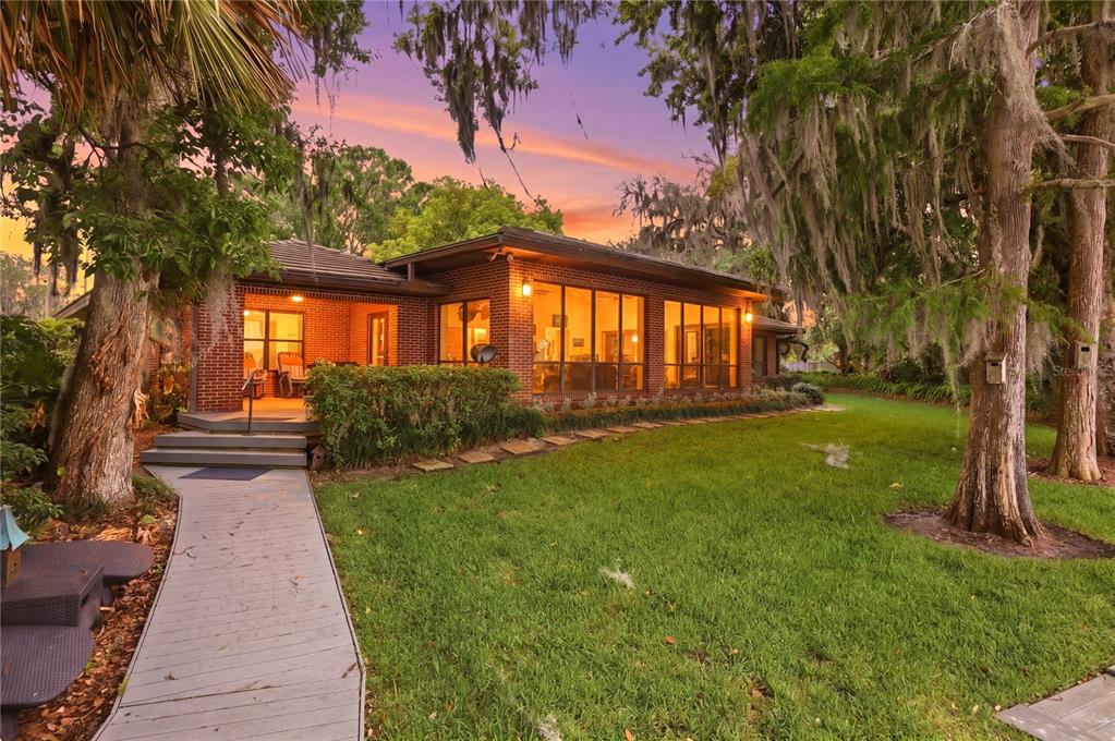 An aerial view shows a waterfront property with a dock, tennis court, and dense trees — 4910 E LAKE DRIVE, WINTER SPRINGS, FL