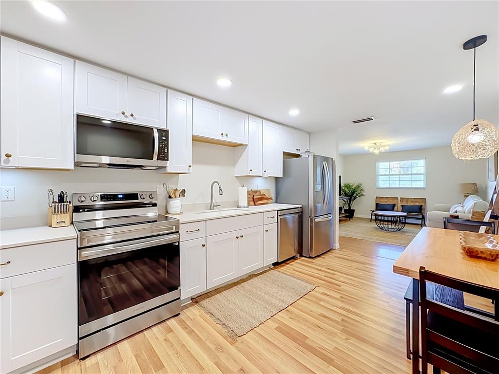 A kitchen with white cabinets, stainless steel appliances, and wood flooring opens into a living area — 202 PEACOCK  UNIT B LANE UNIT B, HOLMES BEACH, FL