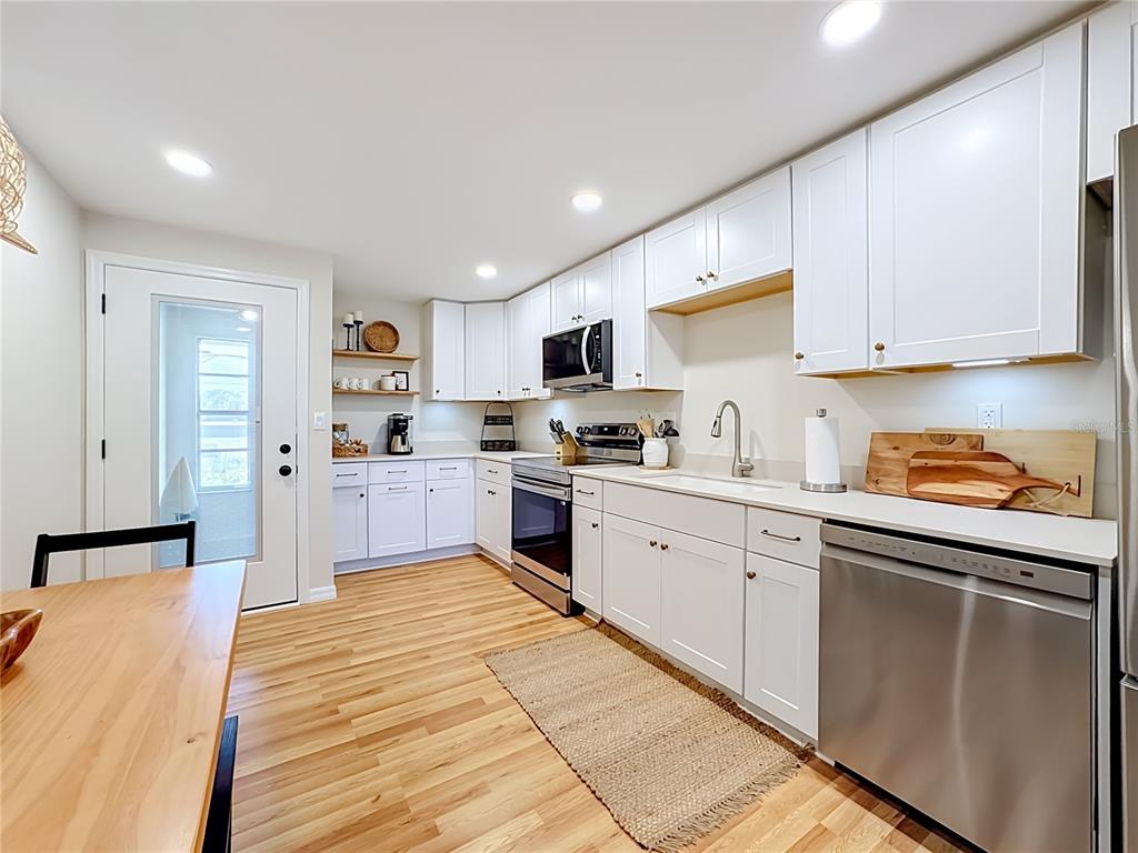 A kitchen features white cabinetry, stainless steel appliances, light wood flooring, and a glass-paneled door — 202 PEACOCK  UNIT B LANE UNIT B, HOLMES BEACH, FL