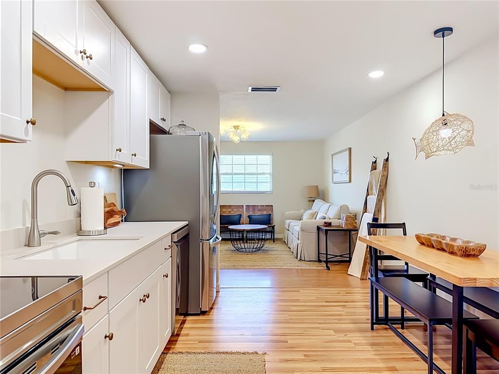 A kitchen with white cabinets and stainless steel appliances opens into a living room area — 202 PEACOCK  UNIT B LANE UNIT B, HOLMES BEACH, FL