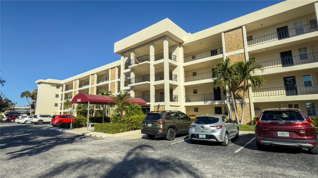 A multi-story apartment building with a red awning entrance and a parking lot in front — 7461 W COUNTRY CLUB DRIVE N UNIT 209, SARASOTA, FL