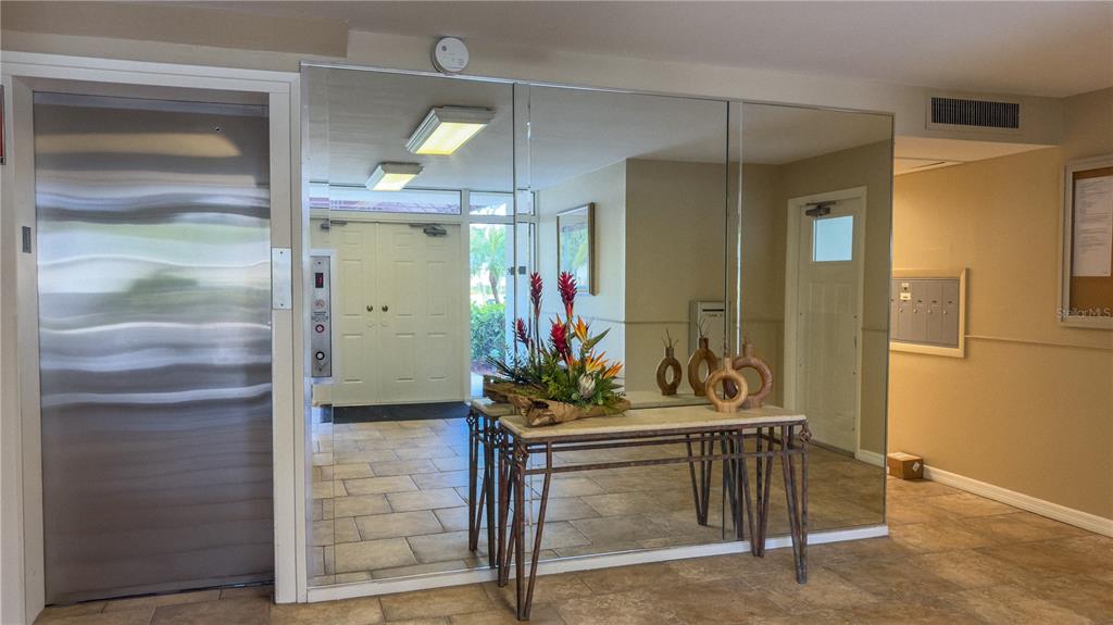 A lobby features a metal elevator door, a mirrored wall, and a console table with flowers — 7461 W COUNTRY CLUB DRIVE N UNIT 209, SARASOTA, FL
