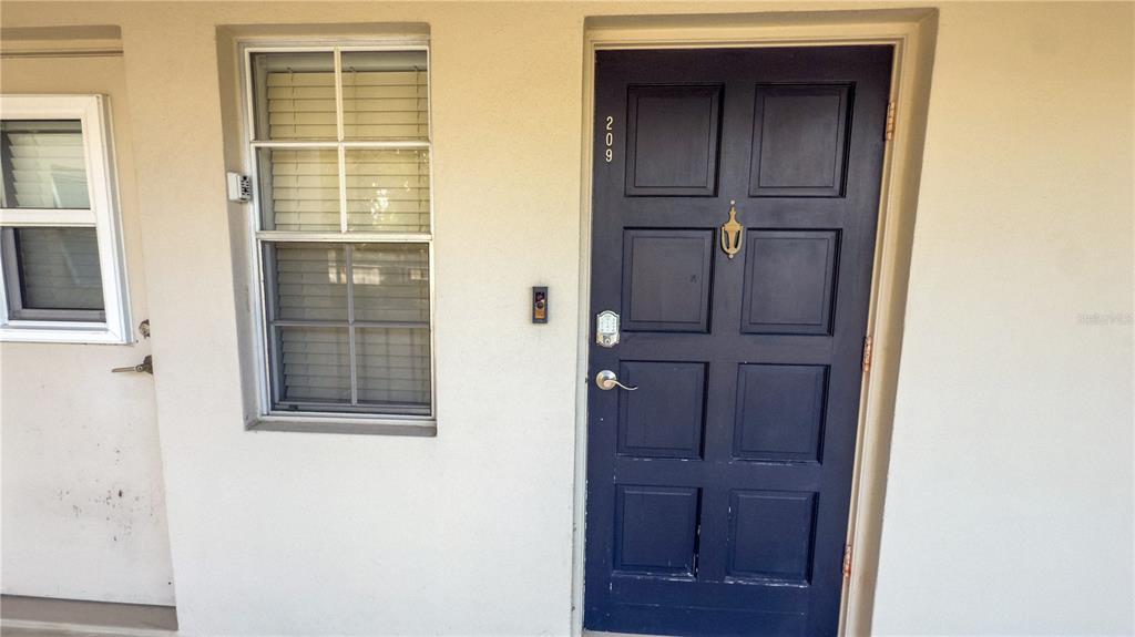A dark blue front door with a brass knocker and keypad lock next to a window — 7461 W COUNTRY CLUB DRIVE N UNIT 209, SARASOTA, FL