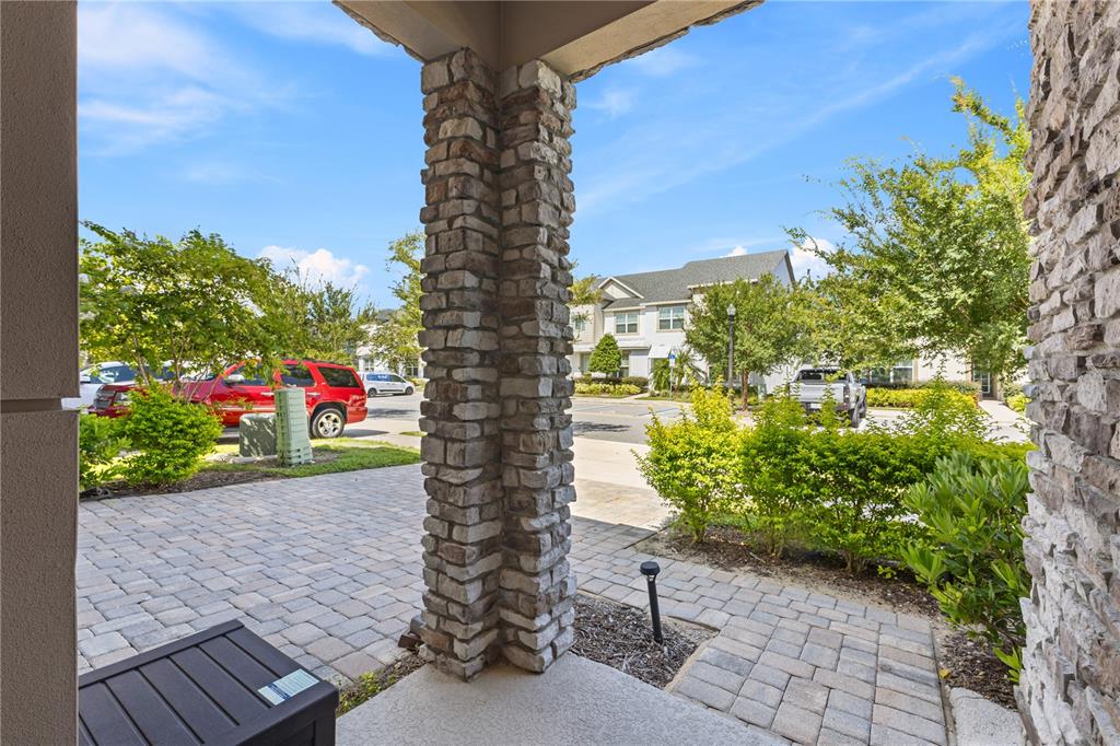 A stone-clad pillar stands on a paved patio overlooking a residential street with parked cars — 8975 AMELIA DOWNS TRAIL, KISSIMMEE, FL