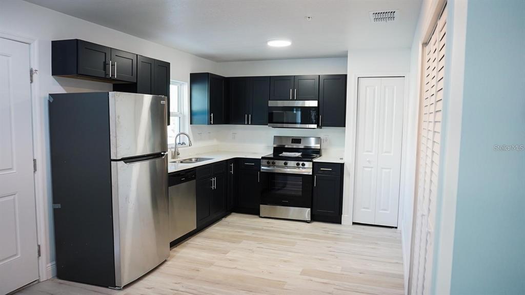A kitchen features dark cabinetry, stainless steel appliances, and light wood-look flooring — 2201 CONWAY DRIVE UNIT 203, DELTONA, FL