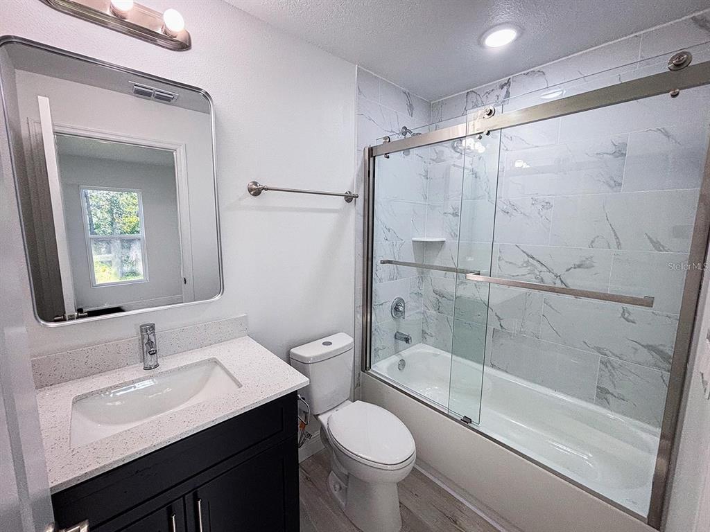 A bathroom features a dark vanity, white countertop, toilet, and a marble-tiled shower enclosure — 2201 CONWAY DRIVE UNIT 203, DELTONA, FL