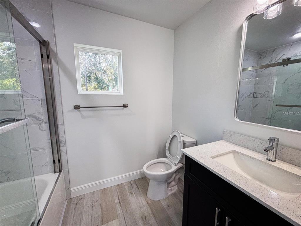 A bathroom features a glass-enclosed shower, a toilet, and a vanity with a stone countertop — 2201 CONWAY DRIVE UNIT 203, DELTONA, FL