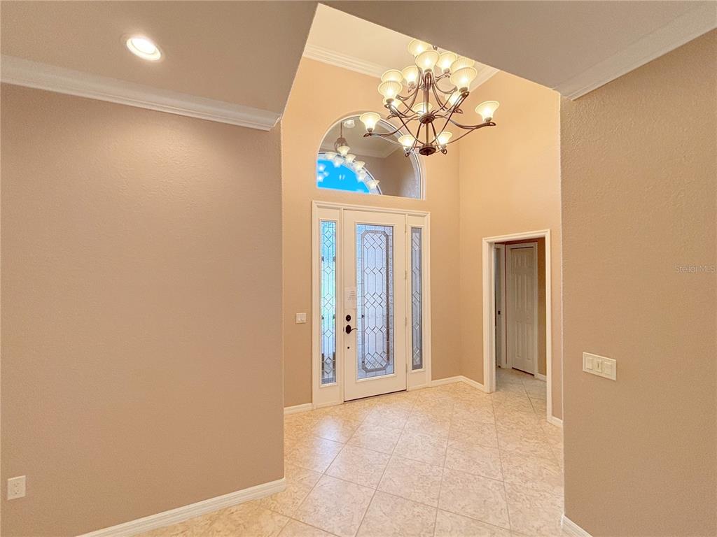 An entryway with a high ceiling, chandelier, tiled floor, and a decorative glass front door — 4577 BACK NINE DRIVE, WINTER HAVEN, FL