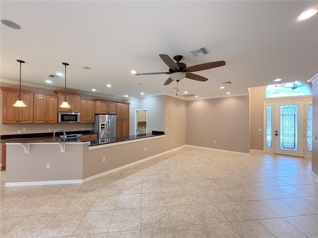 A kitchen with dark countertops and wood cabinets overlooks an open-concept living area with tile floors — 4577 BACK NINE DRIVE, WINTER HAVEN, FL