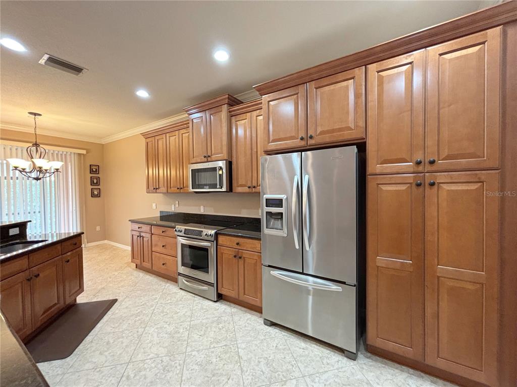 A kitchen features wood cabinets, stainless steel appliances, dark countertops, and tile flooring — 4577 BACK NINE DRIVE, WINTER HAVEN, FL