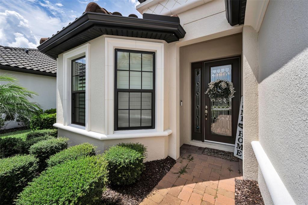 The exterior of a house features a bay window, a dark front door, and a brick walkway — 11386 JUGLANS DRIVE, ODESSA, FL