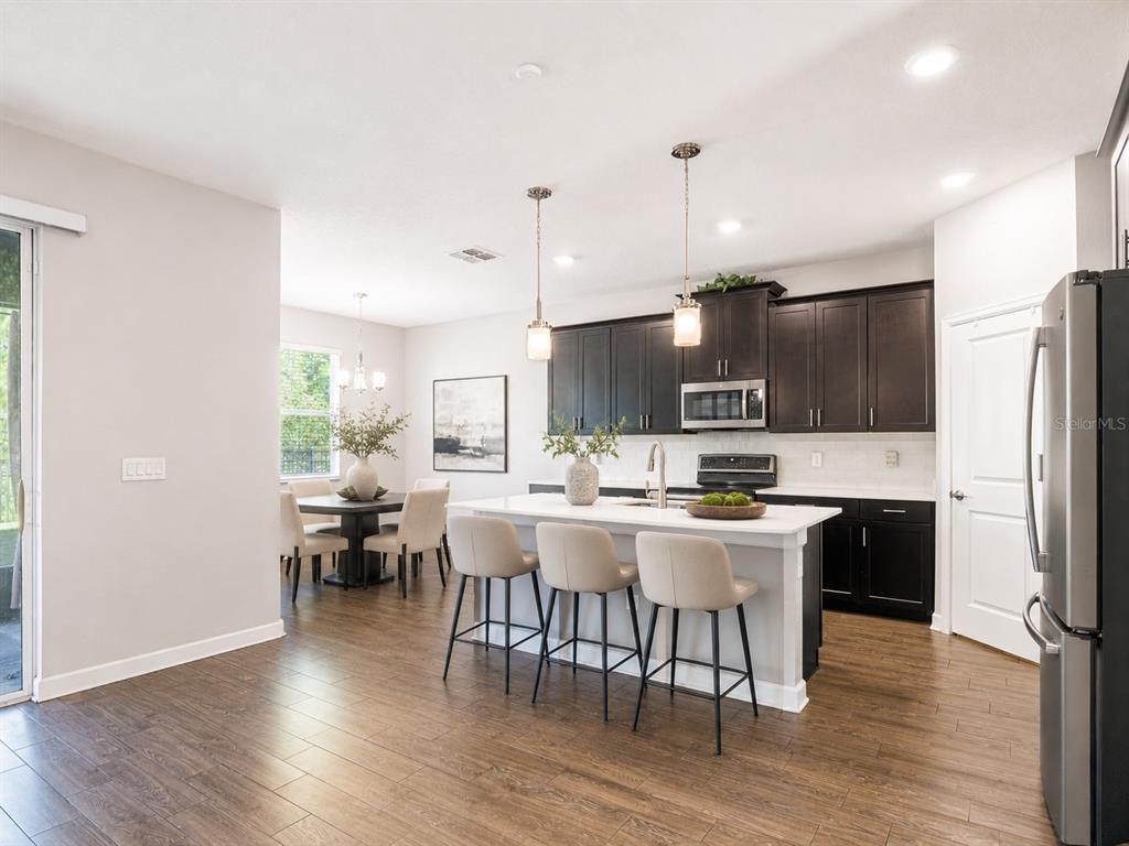 An open-concept living and dining area features wood-look tile flooring and a view of the kitchen — 491 BRUNSWICK DRIVE, DAVENPORT, FL