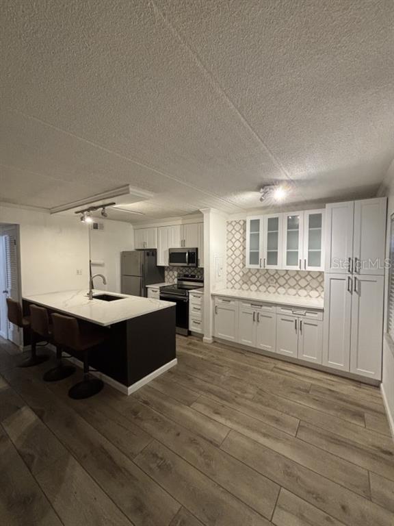 A modern kitchen features white cabinetry, a dark kitchen island with seating, and wood-look flooring — 109 S OBRIEN STREET UNIT 123, TAMPA, FL