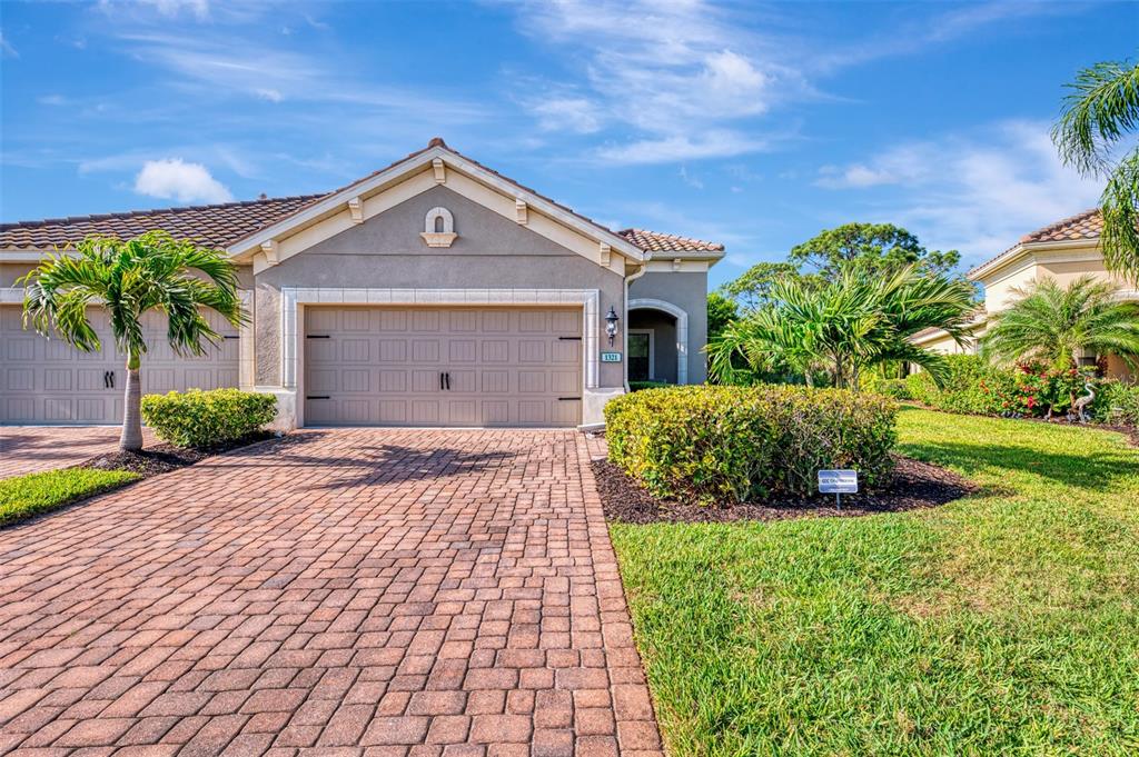 A single-story house with a beige stucco exterior, a two-car garage, and a brick driveway — 1321 BACKSPIN DRIVE, ENGLEWOOD, FL